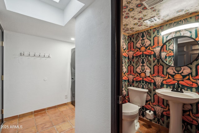 half bathroom featuring baseboards, toilet, visible vents, a skylight, and a sink