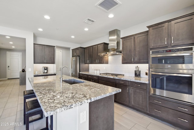 kitchen with visible vents, stainless steel appliances, decorative backsplash, a kitchen breakfast bar, and wall chimney exhaust hood