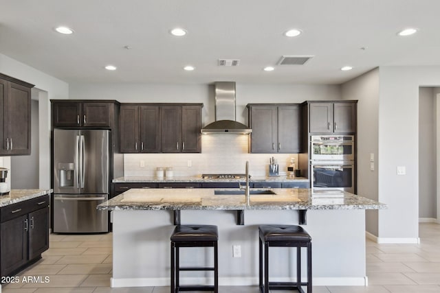 kitchen with wall chimney exhaust hood, visible vents, appliances with stainless steel finishes, and a sink