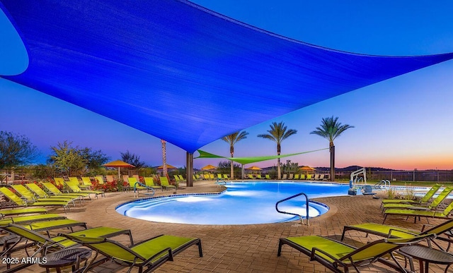 pool at dusk with a patio area, a community pool, and fence