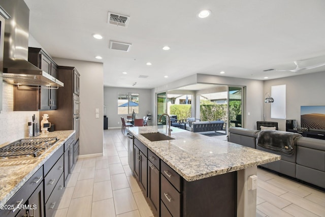 kitchen with a sink, visible vents, wall chimney exhaust hood, and open floor plan