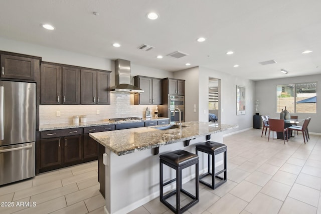 kitchen with visible vents, wall chimney range hood, a center island with sink, decorative backsplash, and appliances with stainless steel finishes