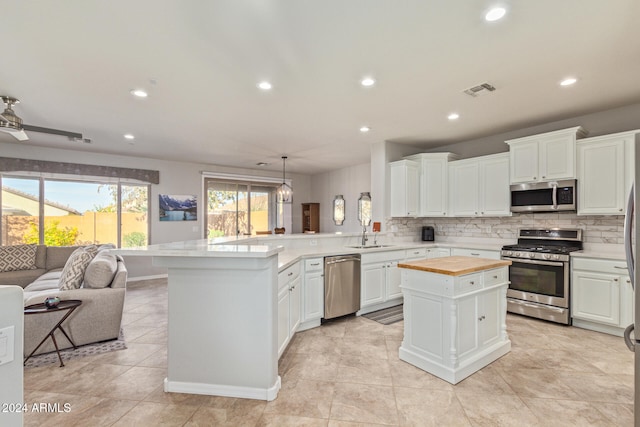 kitchen featuring a center island, appliances with stainless steel finishes, decorative light fixtures, white cabinetry, and kitchen peninsula