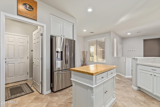 kitchen with wooden counters, light tile patterned floors, white cabinets, stainless steel fridge with ice dispenser, and a kitchen island