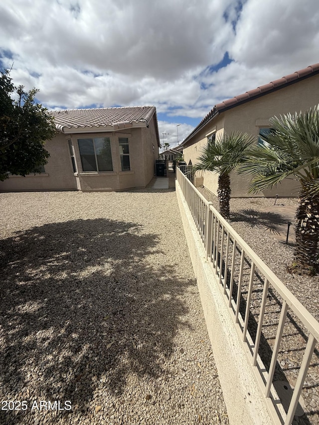 rear view of house featuring a tiled roof, fence, and stucco siding