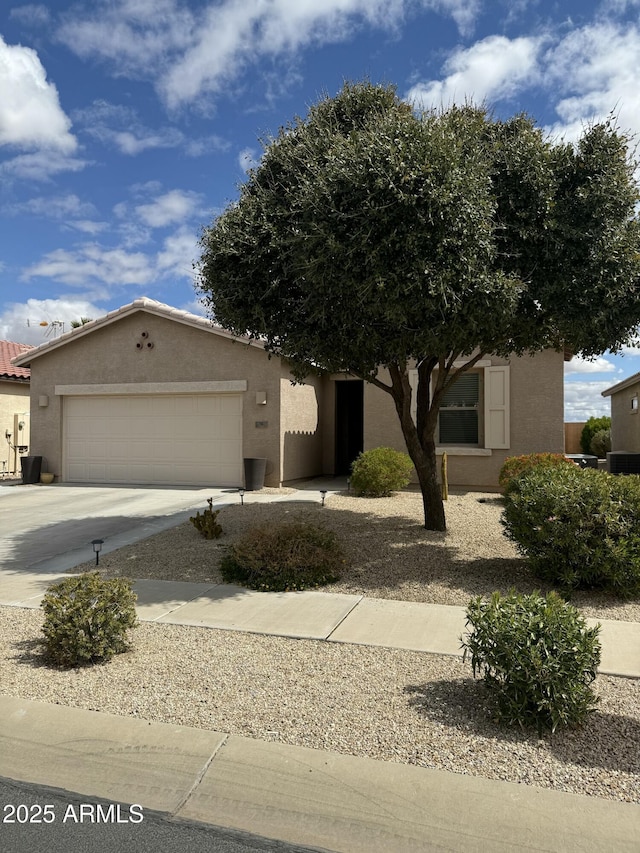 view of property hidden behind natural elements with stucco siding, driveway, and an attached garage