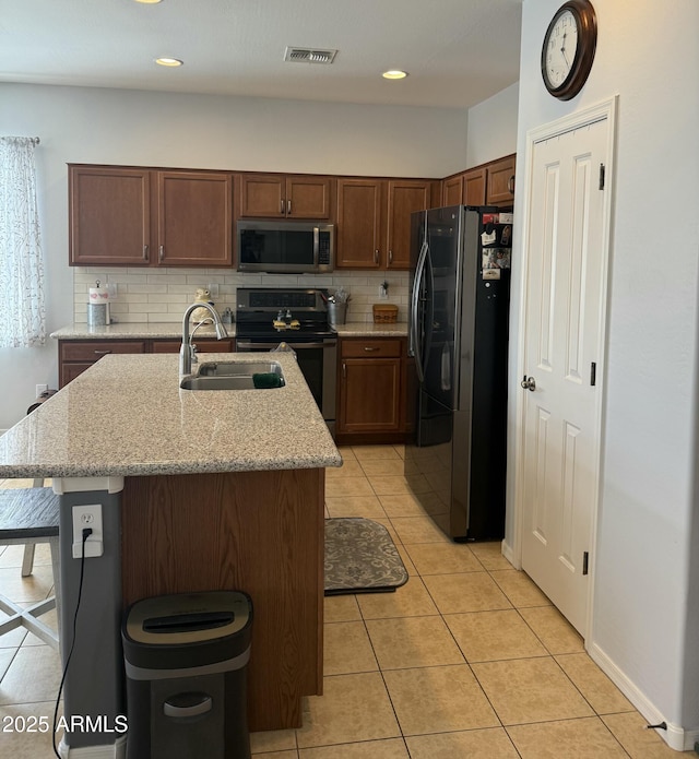 kitchen with visible vents, a center island with sink, a sink, stainless steel appliances, and decorative backsplash