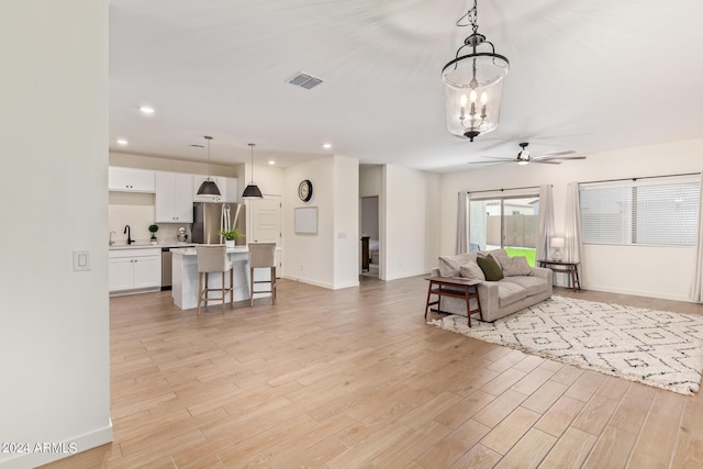 living room with ceiling fan with notable chandelier and light hardwood / wood-style flooring