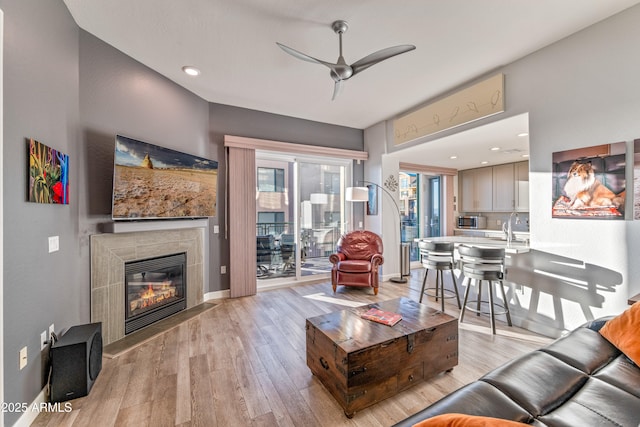 living room with ceiling fan, sink, a fireplace, and light wood-type flooring