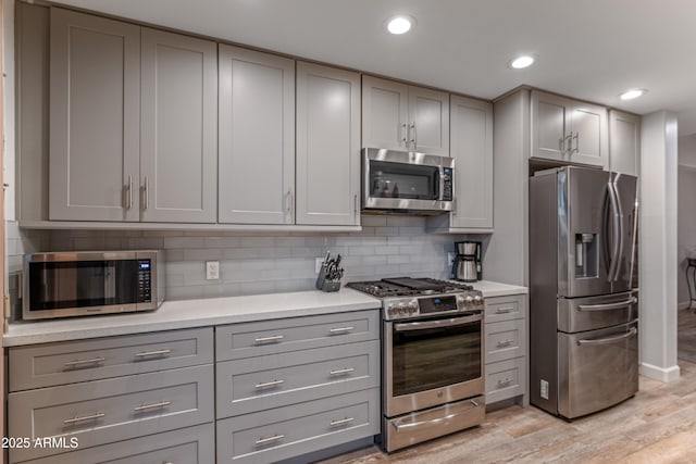 kitchen with tasteful backsplash, gray cabinets, stainless steel appliances, and light hardwood / wood-style flooring