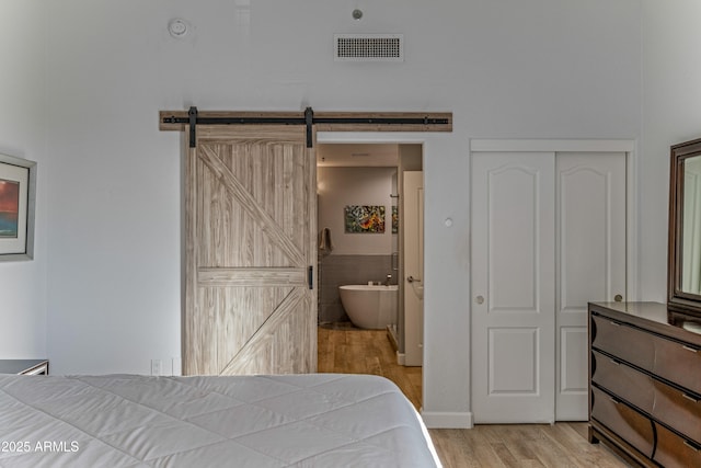 bedroom with light hardwood / wood-style flooring, a barn door, and ensuite bathroom