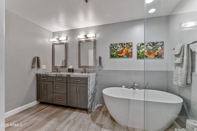 bathroom with wood-type flooring, a tub, tile walls, and vanity