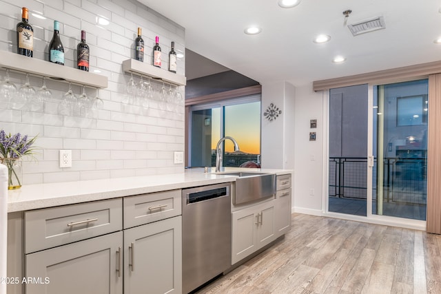 kitchen with gray cabinets, sink, decorative backsplash, stainless steel dishwasher, and light hardwood / wood-style floors