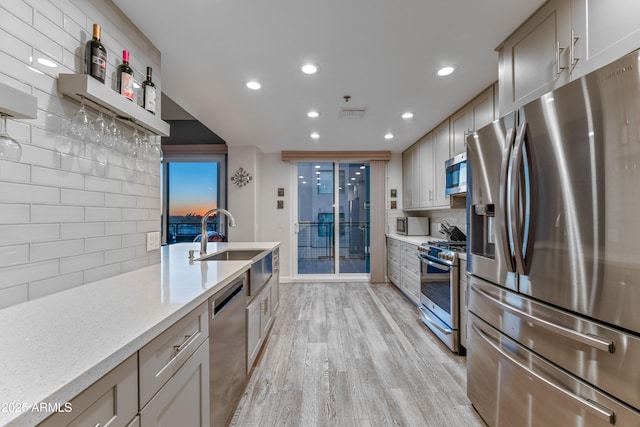 kitchen featuring sink, appliances with stainless steel finishes, backsplash, light stone countertops, and light wood-type flooring