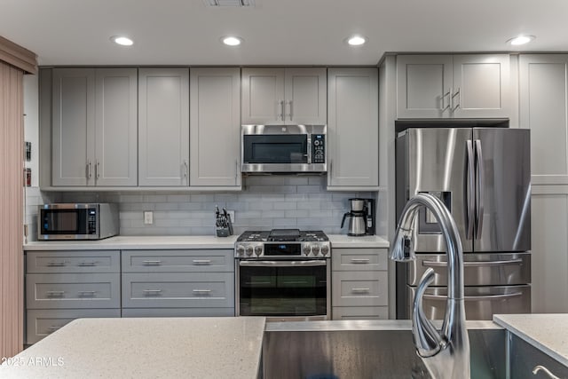 kitchen featuring gray cabinetry, light stone countertops, decorative backsplash, and stainless steel appliances