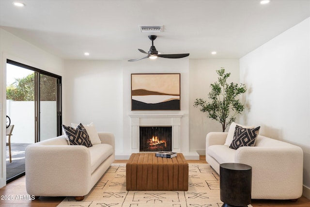 living area with a warm lit fireplace, ceiling fan, recessed lighting, visible vents, and light wood-type flooring