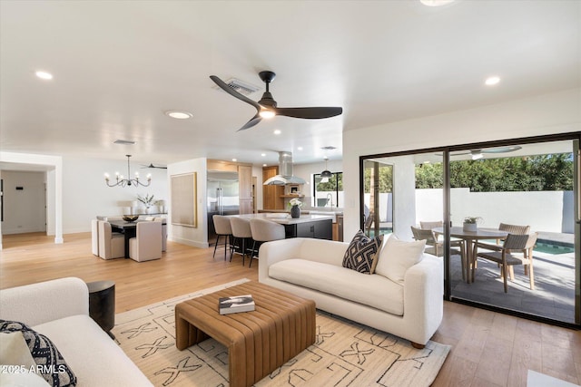 living area with recessed lighting, ceiling fan with notable chandelier, visible vents, baseboards, and light wood-type flooring