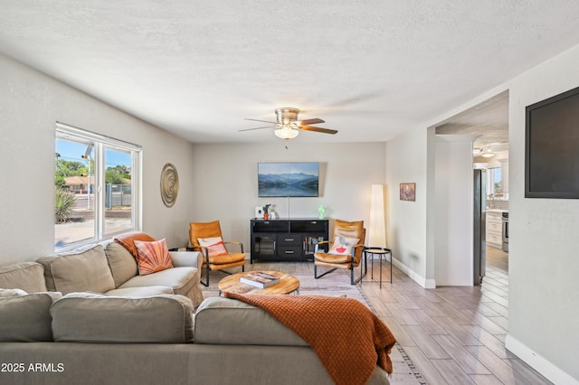 living area featuring baseboards, a ceiling fan, a textured ceiling, and wood finish floors