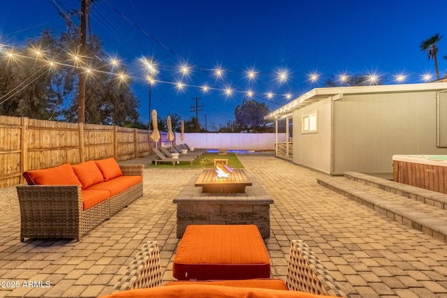 patio at night featuring a hot tub, a fenced backyard, and an outdoor living space with a fire pit