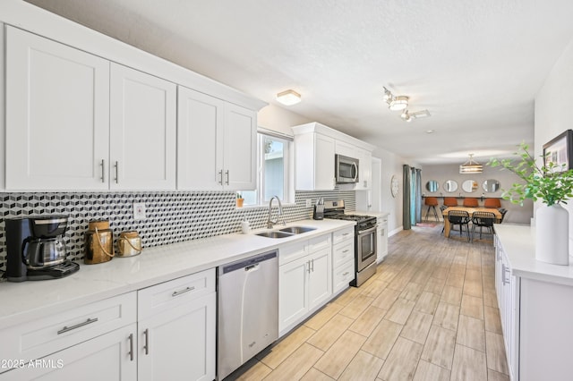 kitchen with white cabinets, appliances with stainless steel finishes, a sink, light countertops, and backsplash