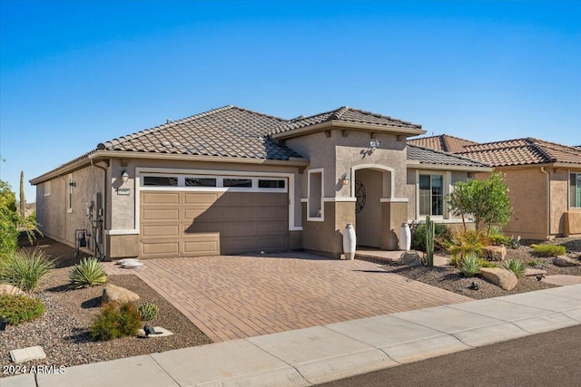 mediterranean / spanish house with a garage, decorative driveway, a tile roof, and stucco siding