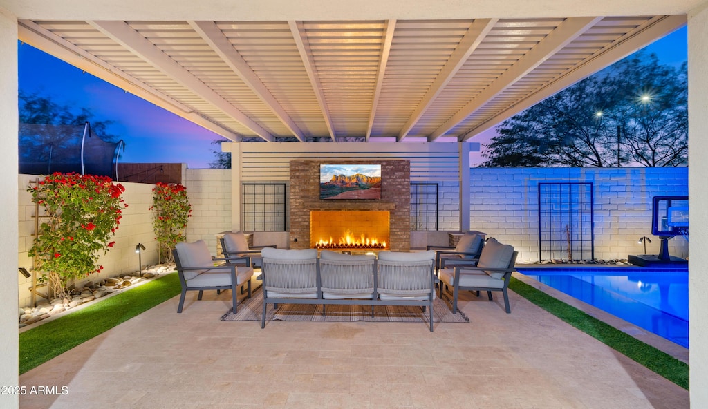 patio terrace at dusk with exterior fireplace and a fenced in pool