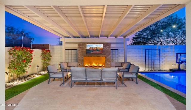 patio terrace at dusk with exterior fireplace and a fenced in pool