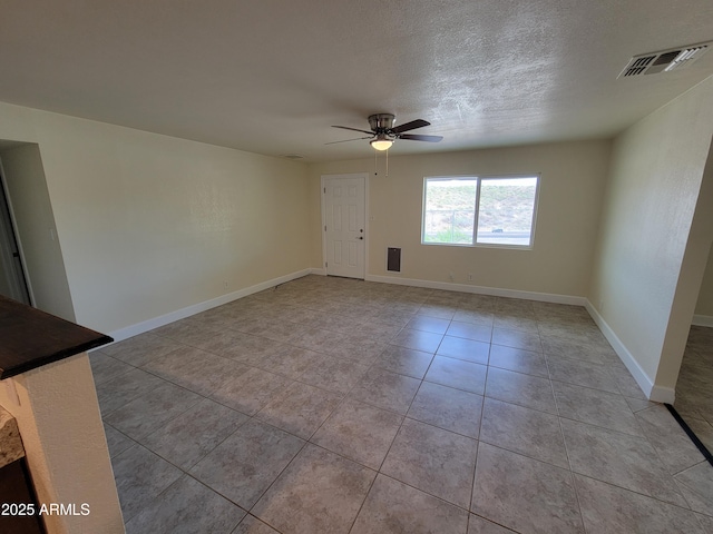 empty room featuring visible vents, a ceiling fan, light tile patterned floors, baseboards, and a textured ceiling