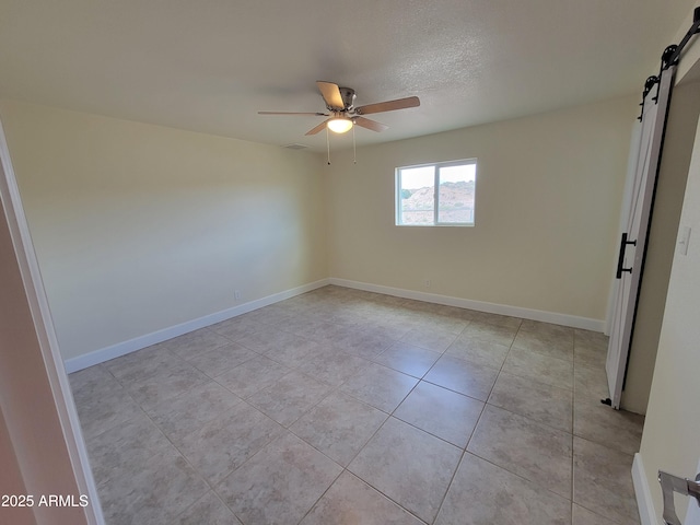 unfurnished room with baseboards, light tile patterned flooring, ceiling fan, and a barn door