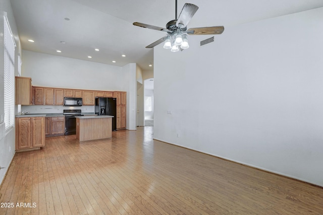 kitchen with black appliances, light hardwood / wood-style floors, a towering ceiling, ceiling fan, and a kitchen island