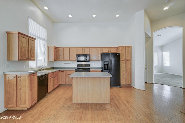 kitchen with black appliances, light hardwood / wood-style floors, a center island, a towering ceiling, and sink