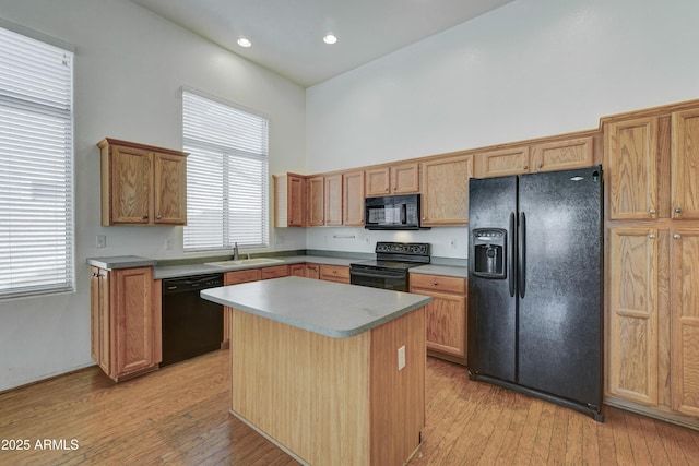 kitchen featuring a healthy amount of sunlight, a center island, a high ceiling, black appliances, and sink