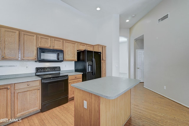 kitchen featuring a towering ceiling, light hardwood / wood-style floors, a center island, and black appliances