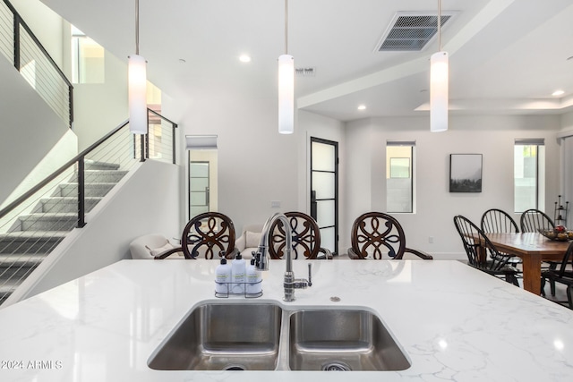 kitchen with hanging light fixtures, light stone countertops, and sink