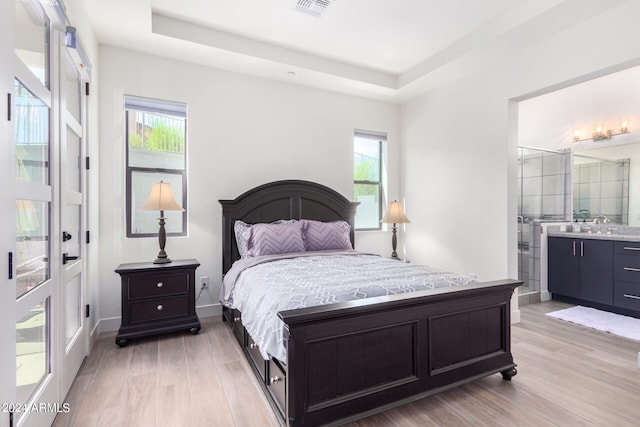 bedroom featuring light wood-type flooring, ensuite bath, a raised ceiling, and sink