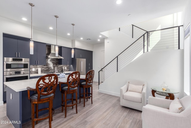 kitchen featuring hanging light fixtures, decorative backsplash, wall chimney exhaust hood, a kitchen bar, and light hardwood / wood-style flooring