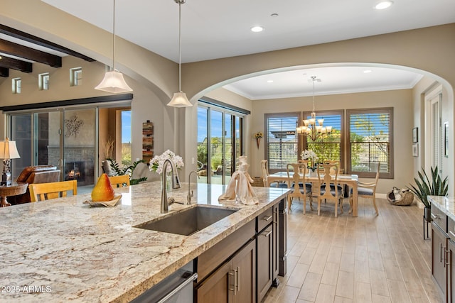 kitchen with light stone countertops, recessed lighting, arched walkways, a sink, and light wood-style floors