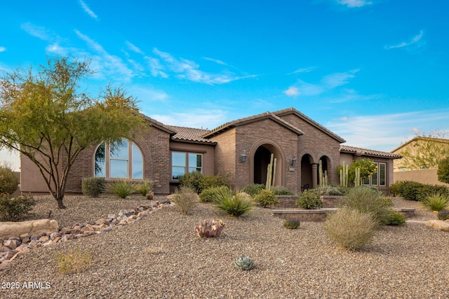 view of front of property with a tile roof, brick siding, and stucco siding