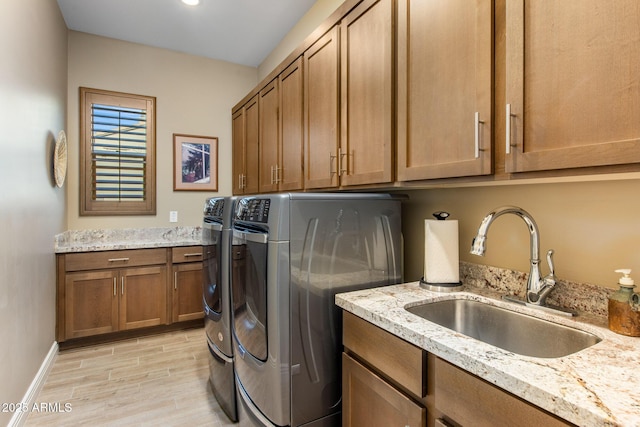 laundry area featuring washing machine and clothes dryer, baseboards, light wood-style floors, cabinet space, and a sink