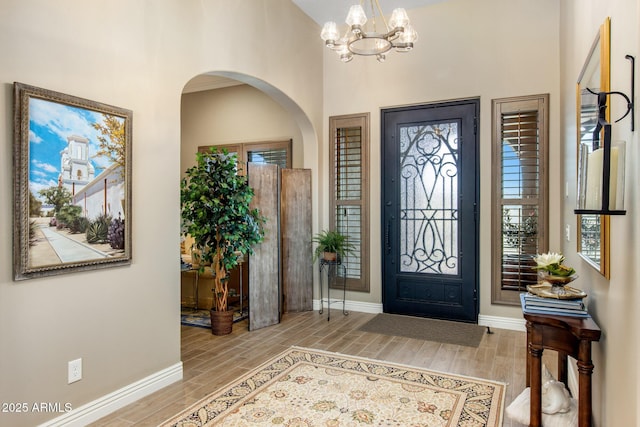 foyer featuring baseboards, wood finish floors, an inviting chandelier, arched walkways, and a towering ceiling