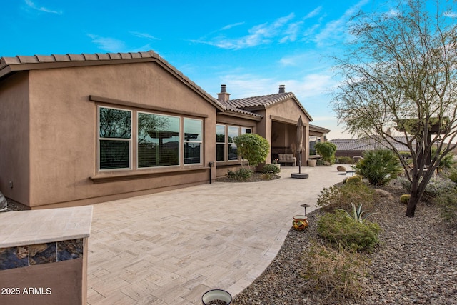 rear view of property with stucco siding, a tile roof, a patio, and fence