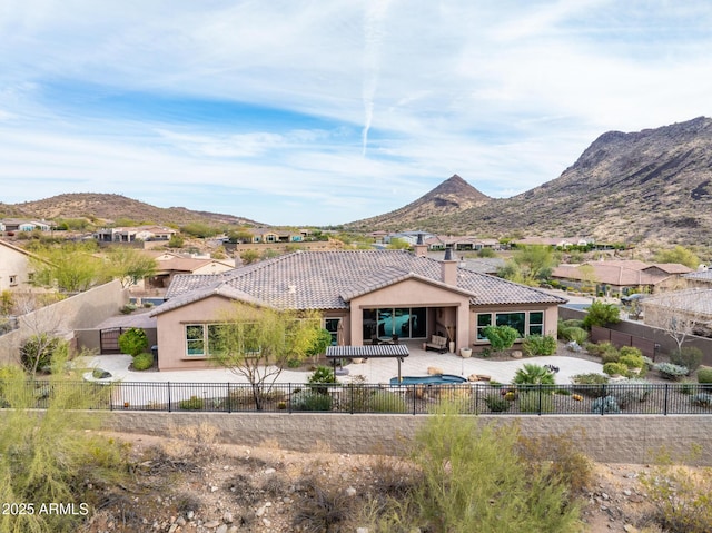 back of house with a tile roof, a fenced backyard, a mountain view, and a chimney