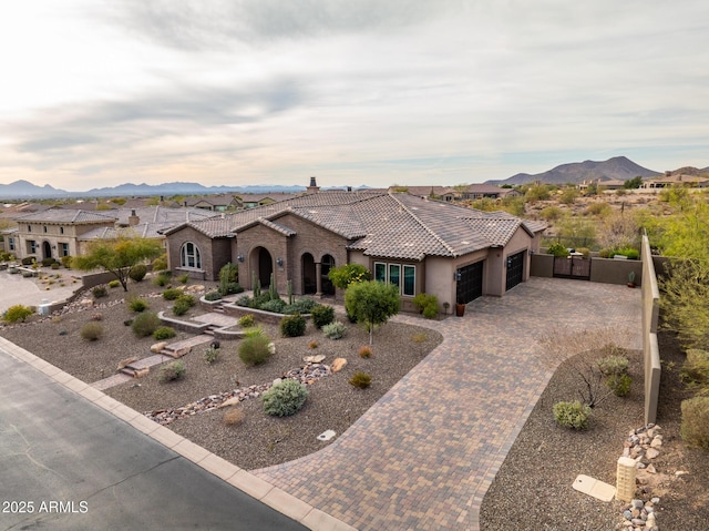 mediterranean / spanish-style home featuring decorative driveway, fence, a mountain view, an attached garage, and a tiled roof
