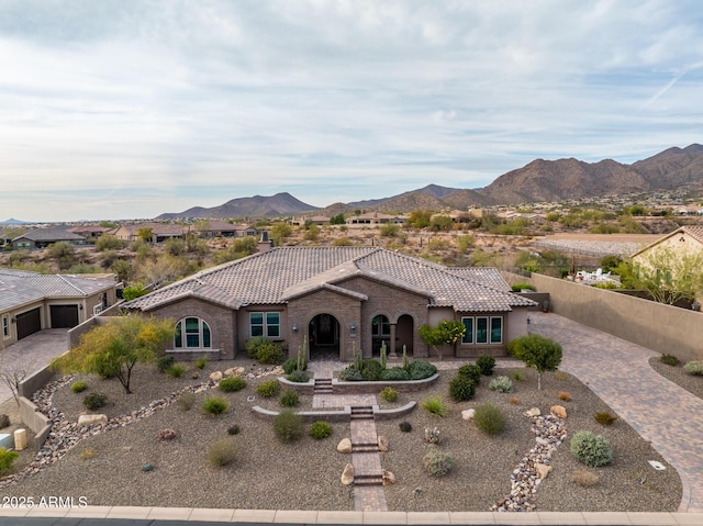 mediterranean / spanish-style home featuring stucco siding, decorative driveway, fence, a mountain view, and a tiled roof