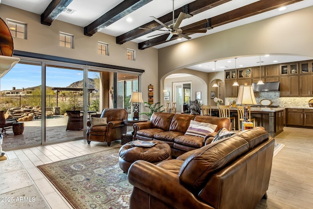 living area featuring a ceiling fan, visible vents, beam ceiling, arched walkways, and a towering ceiling