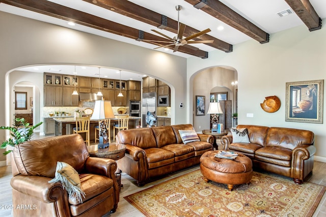living room with arched walkways, visible vents, beamed ceiling, and a ceiling fan