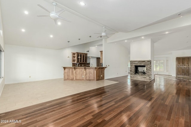 unfurnished living room featuring a stone fireplace, wood-type flooring, and high vaulted ceiling