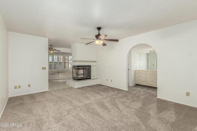 unfurnished living room featuring a multi sided fireplace, light carpet, and ceiling fan