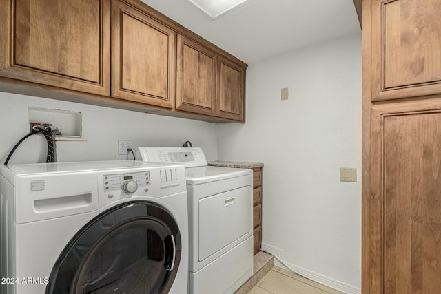 clothes washing area with washing machine and clothes dryer, light tile patterned flooring, and cabinets