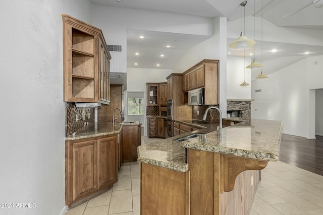 kitchen with light stone countertops, backsplash, kitchen peninsula, lofted ceiling, and decorative light fixtures